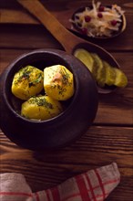 Baked potato in old pot on wooden background with pickled cabbage and cucumber