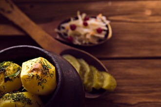 Baked potato in old pot on wooden background with pickled cabbage and cucumber