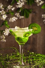 Kiwi fruit soft drink cocktail with ice on a wooden background with flowers