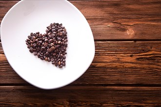 Grains of roasted coffee in the shape of heart on a white plate