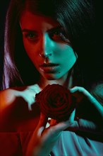 Beautiful girl with a rose in her hand. The beauty of the face. Portrait shot in studio with color filters