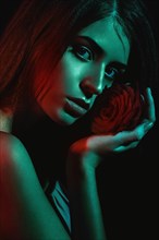 Beautiful girl with a rose in her hand. The beauty of the face. Portrait shot in studio with color filters