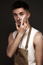 Handsome man hairdresser in a working uniform with scissors in his hands. Photo taken in the studio