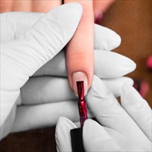 Closeup finger nail care by manicure specialist in beauty salon. Manicurist paints nails with red nail polish