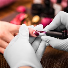 Closeup finger nail care by manicure specialist in beauty salon. Manicurist paints nails with red nail polish