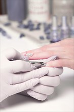 Closeup finger nail care by manicure specialist in beauty salon. Manicurist paints nails with nail polish