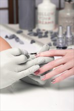 Closeup finger nail care by manicure specialist in beauty salon. Manicurist paints nails with nail polish