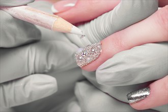 Closeup finger nail care by manicure specialist in beauty salon. Manicurist Glues rhinestones on nails