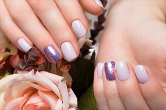 Purple neat manicure on female hands on a background of flowers. Nail design