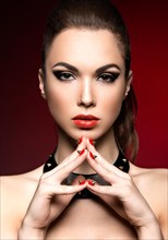 Beautiful woman in gothic style with evening makeup and red nails with thorns. Picture taken in a studio on a red background