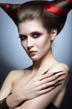 The girl in an image of the demon-tempter with long nails and haircut in the form of horns. Picture taken in the studio on a gray background
