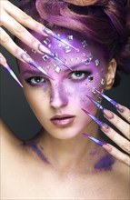 Girl with bright purple creative makeup with crystals and long nails. Beauty face. Picture taken in the studio on a gray background