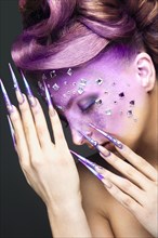 Girl with bright purple creative makeup with crystals and long nails. Beauty face. Picture taken in the studio on a gray background