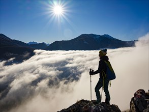 Mountaineer standing exposed above the sea of clouds in sunshine
