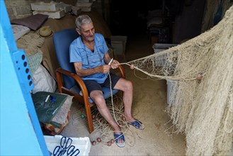 Old fisherman repairing nets