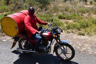 Man rides oil barrel on a motorbike in Kenya
