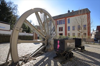 Monument with winding wheel and lorries at mining