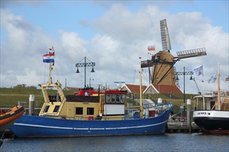 Harbour with ships at the quay wall and windmill in Oudeschild