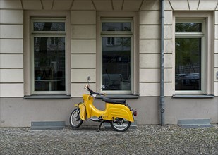 Yellow DDR motor scooter Schwalbe in front of a house facade in Berlin