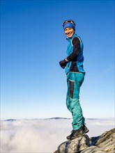 Mountaineer standing exposed on a rock above the clouds