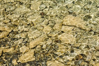 Sun casts fascinating play of light and shadow on the clear water and beige-brown stones on the shore of Lake Walen