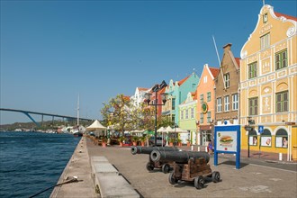 Waterfront at St. Saint Anna Bay in front historical cannons guns right representative houses buildings from colonial times left in the background Queen Juliana Bridge