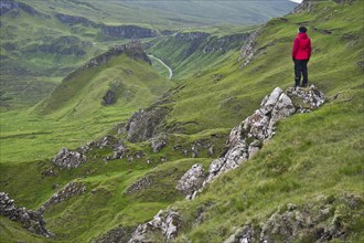 Hiker in red outdoor jacket in the bizarre rock world of Quiraing