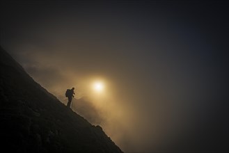 Mountaineer on mountain slope with fog against the light