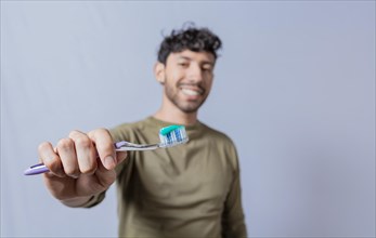 Smiling man showing a toothbrush in the foreground. Smiling young man showing toothbrush with toothpaste isolated. Smiling people holding toothbrush with toothpaste with copy space