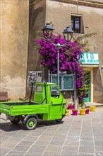 Green Piaggio Ape utility vehicle in front of the cathedral of Rio nell Elba