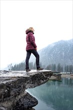 Woman standing on stone in front of foggy lake in winter with snow