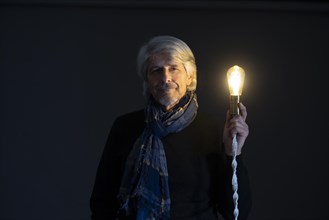 Older gentleman with scarf and shining light bulb smiles