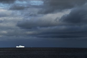 Iceberg drifting on the open sea against a dark cloudy sky