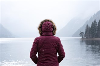 Woman standing in front of foggy lake in winter with snow
