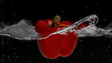 A red pepper falls through a water surface and creates a vortex