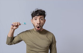 Surprised young man holding a toothbrush with toothpaste. Amazed young man holding toothbrush with toothpaste isolated