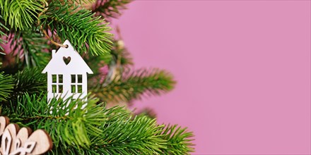 Banner with Christmas tree decorated with white house shaped tree ornament baubles on pink background with empty copy space
