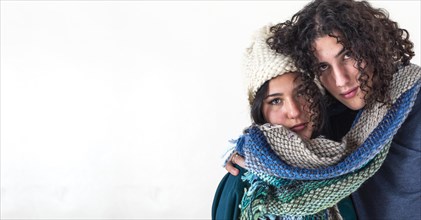 Two friends are hugging each other like they are cold while wearing the same scarf. Winter concept