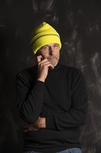 Elderly man in yellow winter cap ponders