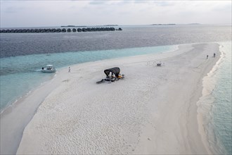 Aerial view: lonely sandbank in the Maldives with a table and sun loungers for romantic dinners
