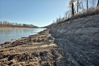 Steep wall of sand and dredge marks on a river bank