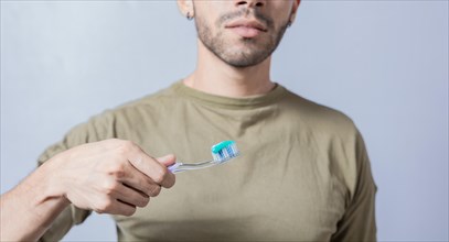 Guy with unrecognizable face holds brush with toothpaste on isolated background