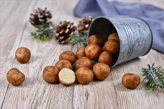 Traditional German Christmas sweets called Marzipankartoffeln. Round ball shaped almond paste pieces covered in cinnamon and cocoa powder spilling out of iron cup on wooden background
