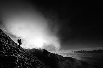 Mountaineer on mountain slope with fog against the light