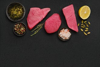 Top view of raw fresh tuna steak and spices on black background