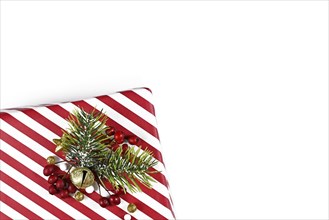 Christmas gift box with red and white striped wrapping paper and seasonal decoration in corner of white background with empty copy space