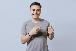 Handsome guy holding and pointing at toothbrush isolated. Person holding and pointing a toothbrush on isolated background