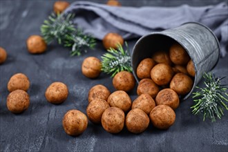 German traditional Christmas sweets called Marzipankartoffeln. Round ball shaped almond paste pieces covered in cinnamon and cocoa powder spilling out of iron cup on dark background