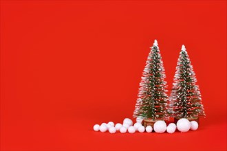 Miniature Christmas trees and snowballs on red background with copy space