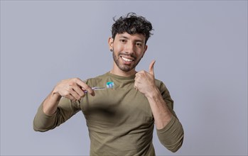 Young man holding a toothbrush with thumb up isolated. Smiling handsome guy holding a toothbrush with thumb up. Smiling people holding toothbrush with thumbs up gesture